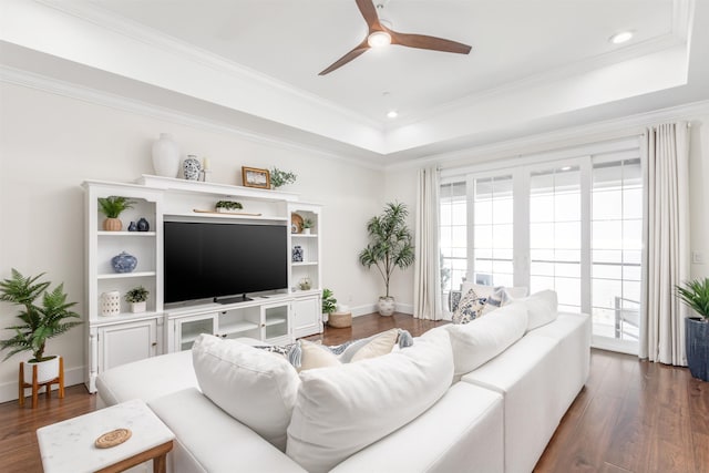 living room with a raised ceiling, ceiling fan, dark hardwood / wood-style flooring, and ornamental molding