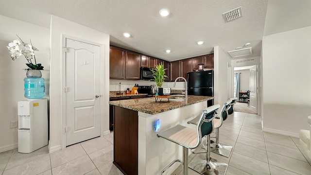 kitchen with a kitchen breakfast bar, a textured ceiling, sink, black appliances, and an island with sink