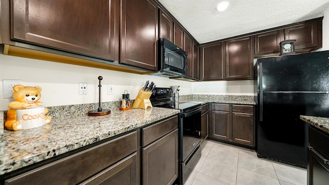 kitchen with black appliances, light tile patterned floors, a textured ceiling, dark brown cabinets, and light stone counters