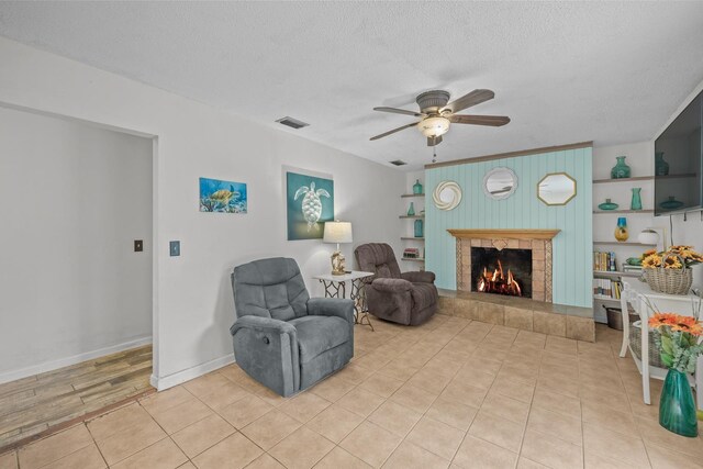 living area with wood walls, a tile fireplace, ceiling fan, a textured ceiling, and light tile patterned flooring