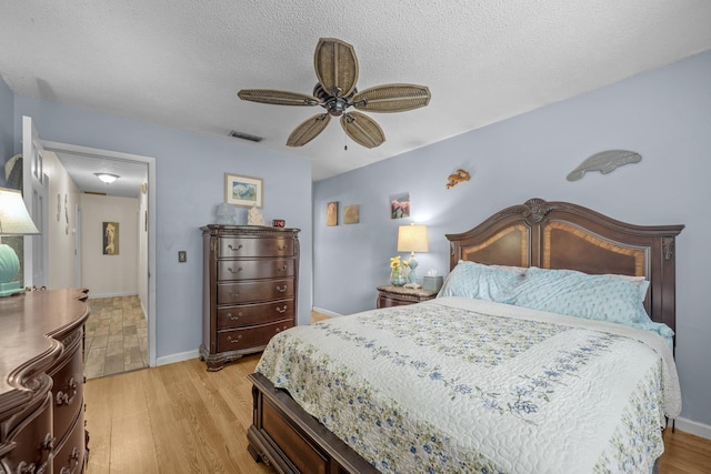 bedroom with ceiling fan, light wood-type flooring, and a textured ceiling