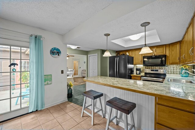 kitchen featuring pendant lighting, black appliances, a kitchen breakfast bar, sink, and a tray ceiling