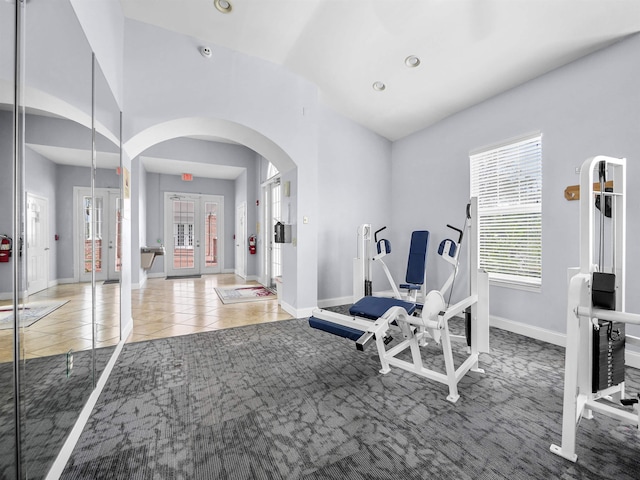 workout room with tile patterned floors, lofted ceiling, recessed lighting, arched walkways, and baseboards