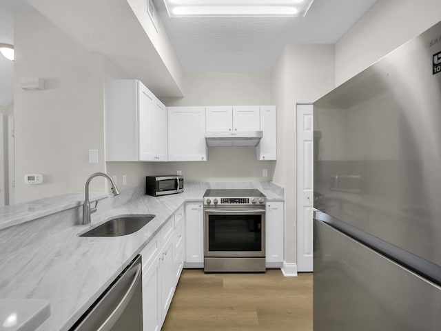 kitchen featuring under cabinet range hood, light wood-style flooring, white cabinets, stainless steel appliances, and a sink