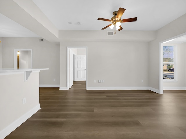 empty room featuring visible vents, baseboards, ceiling fan, and dark wood-style flooring