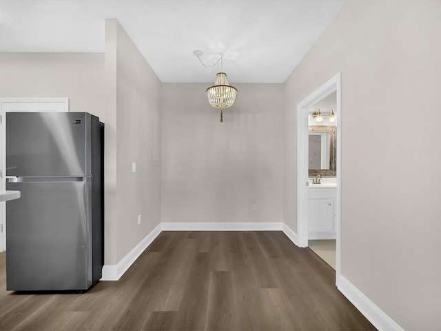 unfurnished dining area with a sink, dark wood-type flooring, baseboards, and a chandelier