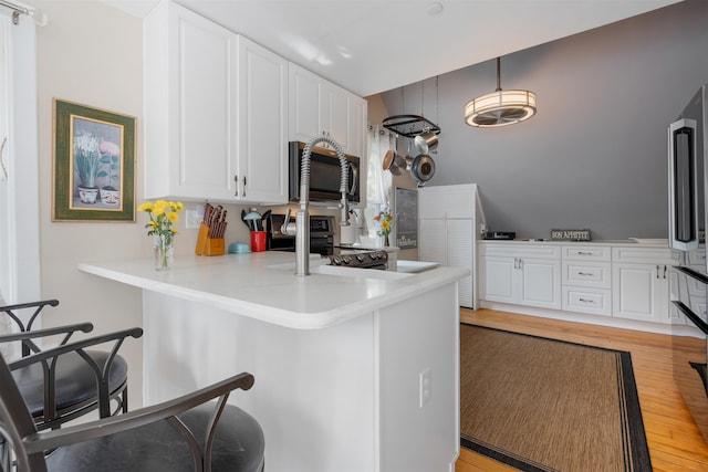 kitchen featuring kitchen peninsula, appliances with stainless steel finishes, white cabinets, and light hardwood / wood-style floors