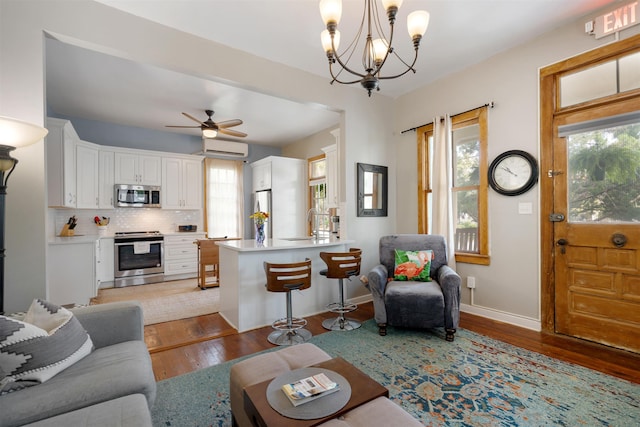 living room featuring an AC wall unit, plenty of natural light, light hardwood / wood-style floors, and ceiling fan with notable chandelier