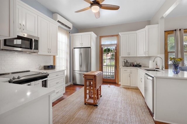 kitchen with sink, appliances with stainless steel finishes, a healthy amount of sunlight, white cabinetry, and a wall unit AC