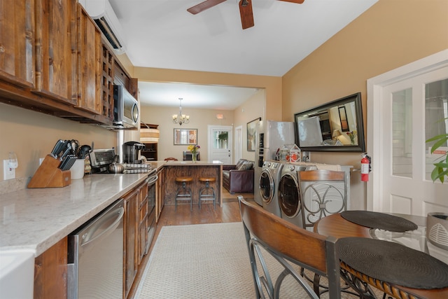 kitchen with dark hardwood / wood-style floors, pendant lighting, washer and dryer, ceiling fan with notable chandelier, and appliances with stainless steel finishes