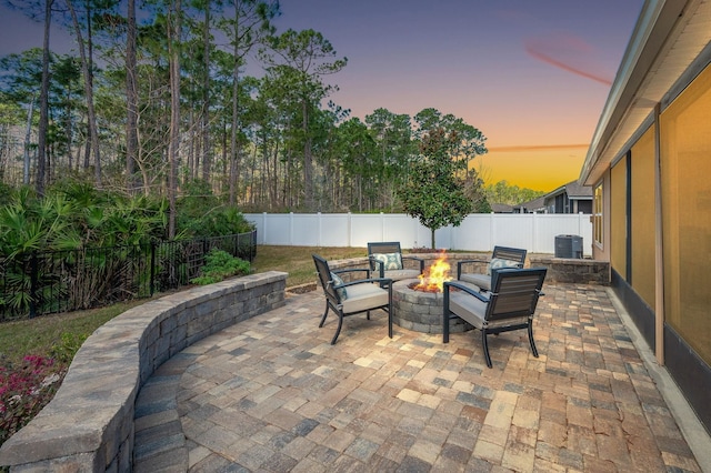 patio terrace at dusk featuring a fire pit, a fenced backyard, and central AC