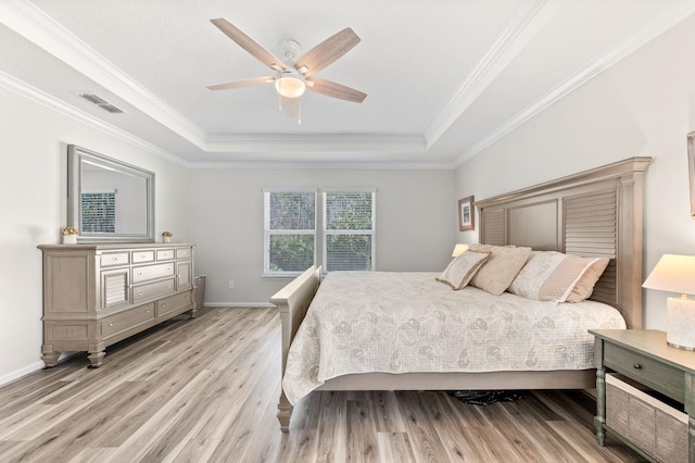 bedroom with light wood-type flooring, a tray ceiling, visible vents, and ornamental molding