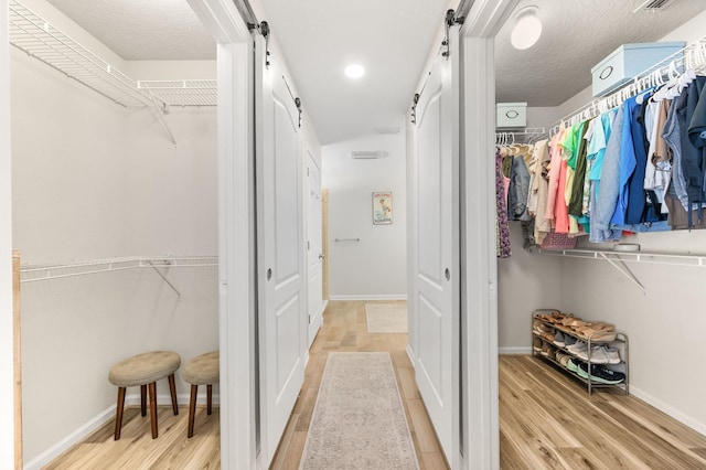 walk in closet with a barn door, visible vents, and wood finished floors