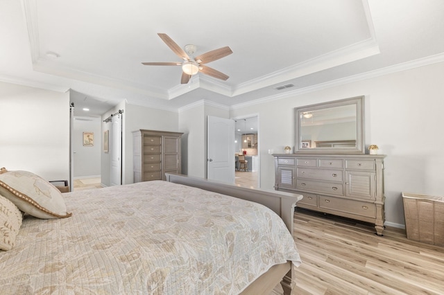 bedroom featuring visible vents, crown molding, a barn door, light wood-style flooring, and a raised ceiling