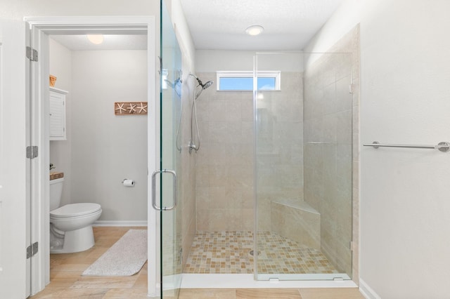 full bathroom with wood finished floors, baseboards, a shower stall, a textured ceiling, and toilet