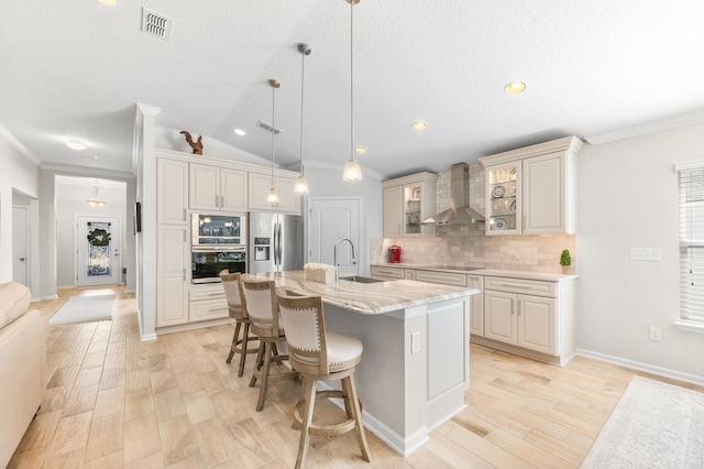 kitchen with a breakfast bar, a sink, appliances with stainless steel finishes, wall chimney exhaust hood, and backsplash