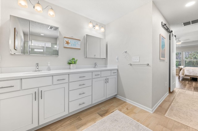 ensuite bathroom with double vanity, visible vents, wood finished floors, and a sink