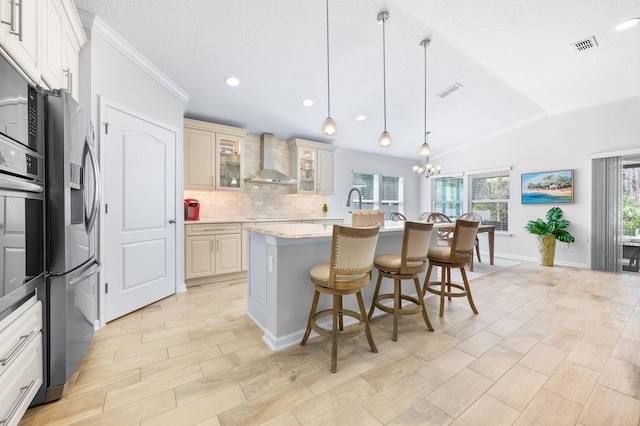 kitchen with an inviting chandelier, stainless steel appliances, a kitchen breakfast bar, wall chimney exhaust hood, and backsplash