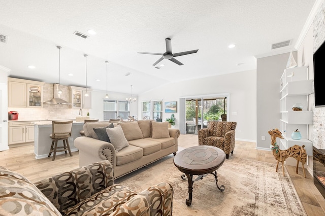 living room featuring visible vents, light wood finished floors, vaulted ceiling, and ceiling fan with notable chandelier