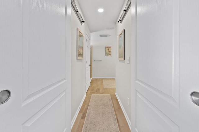 corridor featuring light wood finished floors, recessed lighting, baseboards, and a barn door