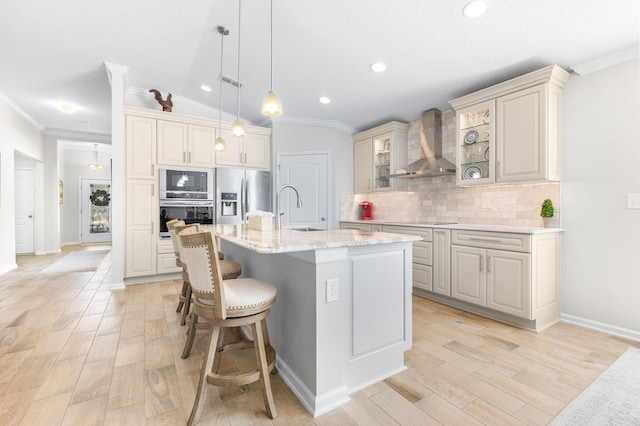 kitchen with a kitchen bar, a sink, backsplash, appliances with stainless steel finishes, and wall chimney exhaust hood