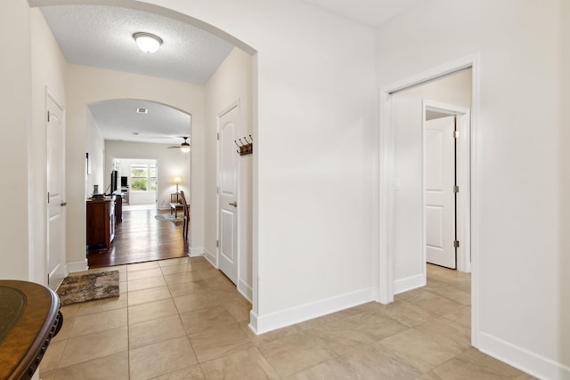 corridor with arched walkways, light tile patterned floors, a textured ceiling, and baseboards