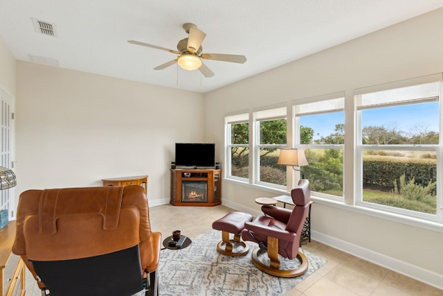 living area featuring light tile patterned flooring, a ceiling fan, visible vents, baseboards, and a glass covered fireplace