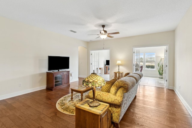 living area with arched walkways, a textured ceiling, wood finished floors, and visible vents