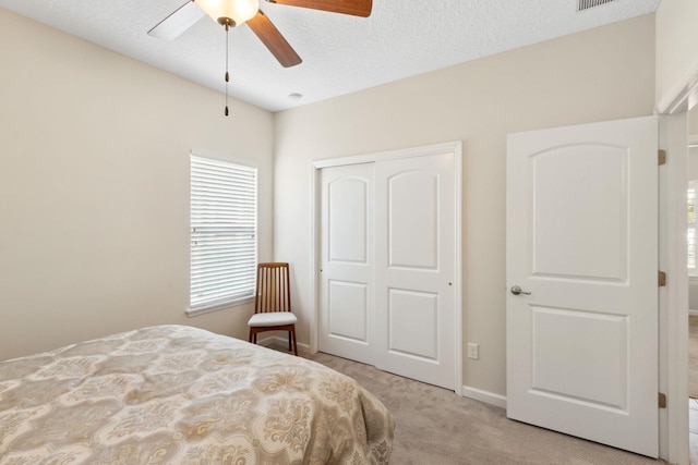 bedroom featuring a closet, a ceiling fan, light carpet, a textured ceiling, and baseboards