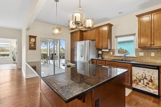 kitchen with a sink, freestanding refrigerator, tasteful backsplash, brown cabinetry, and dark wood finished floors