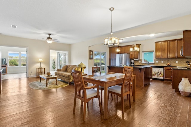 dining space with a healthy amount of sunlight, dark wood-style floors, visible vents, and ceiling fan with notable chandelier