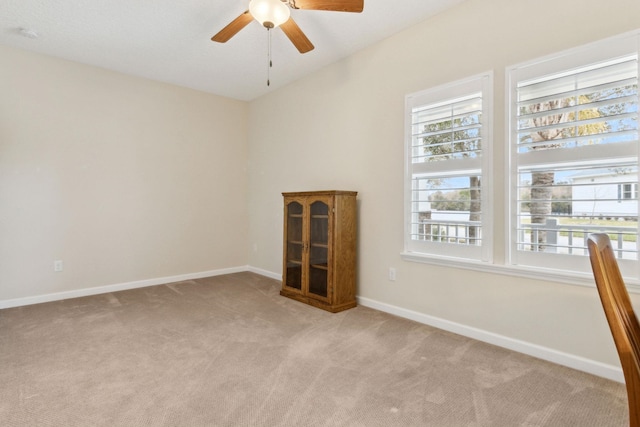 carpeted spare room featuring baseboards and a ceiling fan