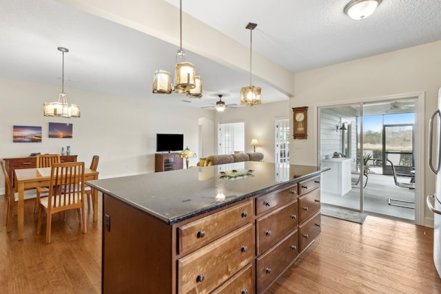 kitchen featuring ceiling fan with notable chandelier, a kitchen island, wood finished floors, and pendant lighting