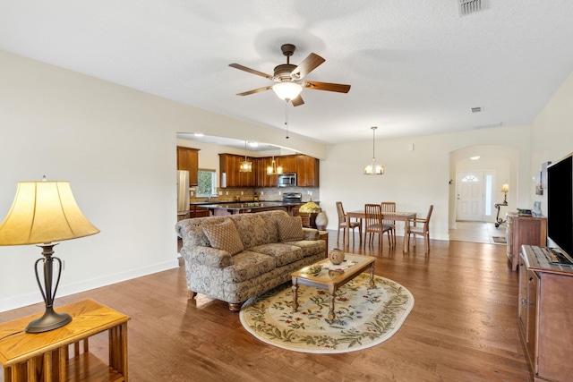 living room featuring arched walkways, ceiling fan with notable chandelier, visible vents, baseboards, and light wood-type flooring