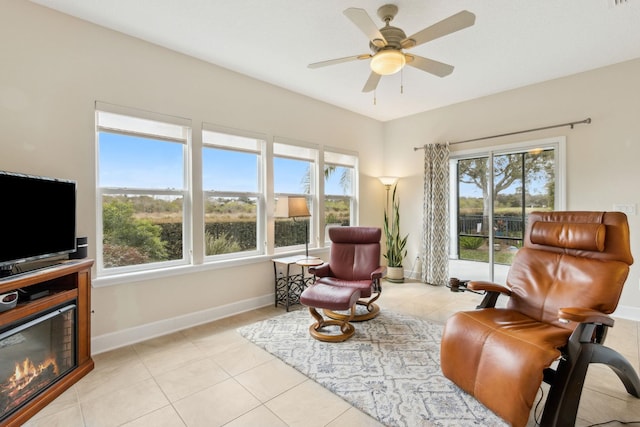 living area featuring light tile patterned floors, visible vents, baseboards, a glass covered fireplace, and ceiling fan