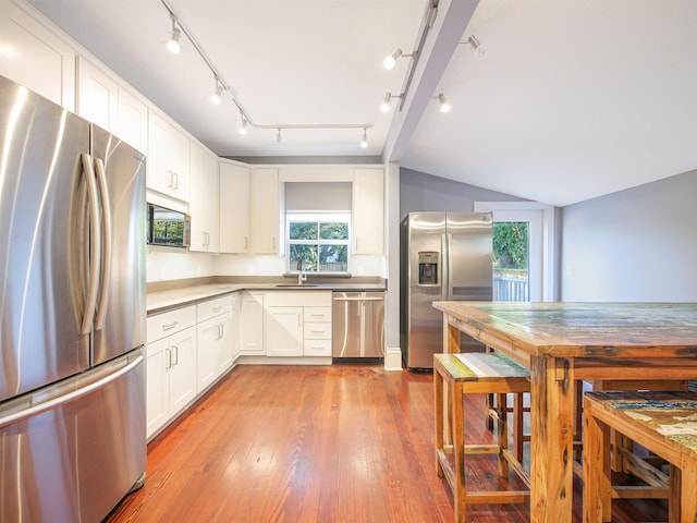 kitchen featuring vaulted ceiling, sink, white cabinets, light hardwood / wood-style floors, and stainless steel appliances