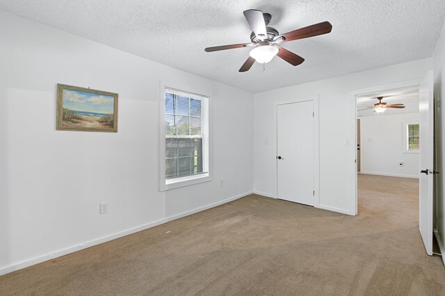 empty room featuring ceiling fan, light colored carpet, and a textured ceiling