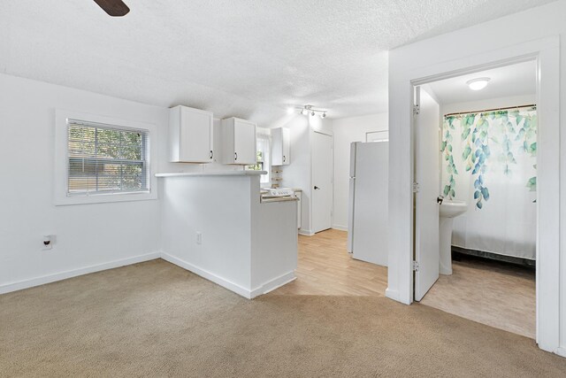 kitchen with white cabinetry, kitchen peninsula, white fridge, a textured ceiling, and light carpet