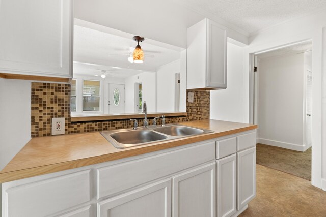 kitchen with light carpet, backsplash, ceiling fan, sink, and white cabinetry