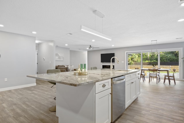 kitchen featuring ceiling fan, an island with sink, pendant lighting, white cabinets, and light wood-type flooring