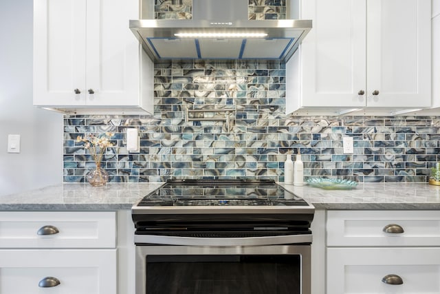 kitchen featuring white cabinetry, electric range, wall chimney exhaust hood, light stone counters, and backsplash