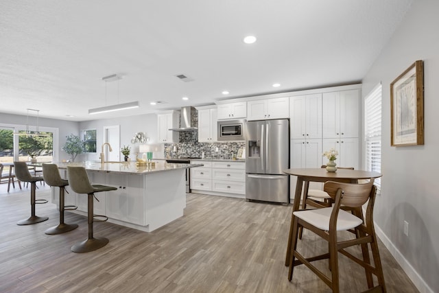 kitchen featuring appliances with stainless steel finishes, white cabinetry, hanging light fixtures, and wall chimney range hood