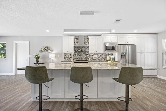 kitchen with a breakfast bar, appliances with stainless steel finishes, white cabinetry, and light stone counters