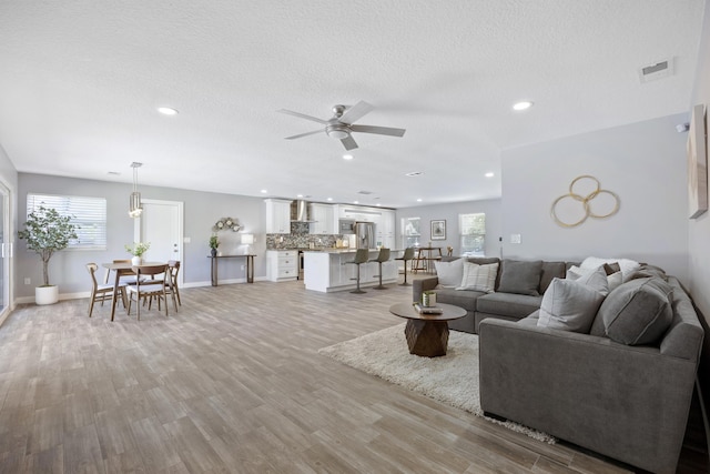 living room with a textured ceiling, light wood-type flooring, a wealth of natural light, and ceiling fan