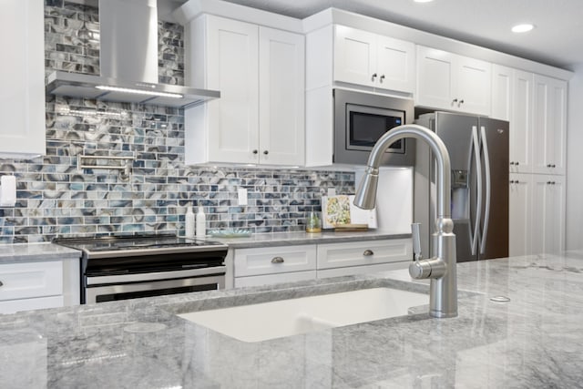 kitchen with white cabinetry, light stone counters, wall chimney exhaust hood, and stainless steel appliances