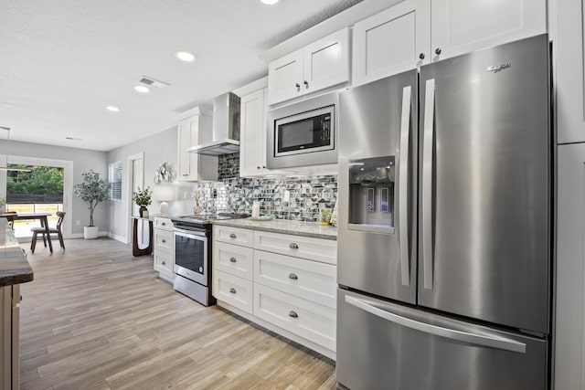 kitchen featuring white cabinets, appliances with stainless steel finishes, light hardwood / wood-style floors, and wall chimney exhaust hood