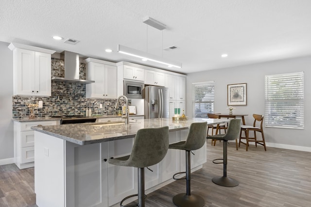 50 Dufferin St, Saint Augustine, FL 32084 - kitchen featuring wall chimney range hood, stainless steel appliances, a kitchen island with sink, decorative backsplash, and a kitchen bar