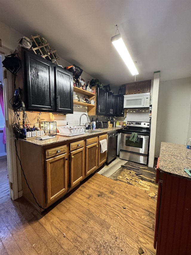 kitchen with light stone countertops, appliances with stainless steel finishes, light wood-type flooring, backsplash, and sink