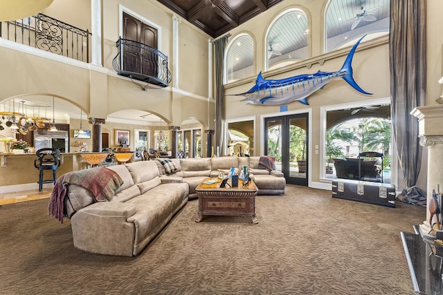 carpeted living room featuring ornate columns, ceiling fan, french doors, and a towering ceiling