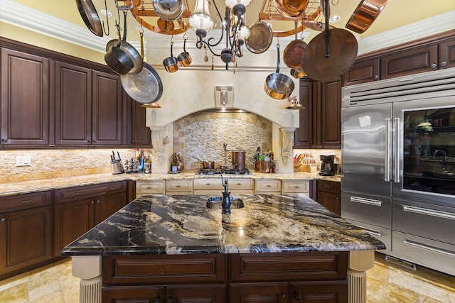 kitchen with tasteful backsplash, stainless steel appliances, a kitchen island with sink, crown molding, and dark stone countertops